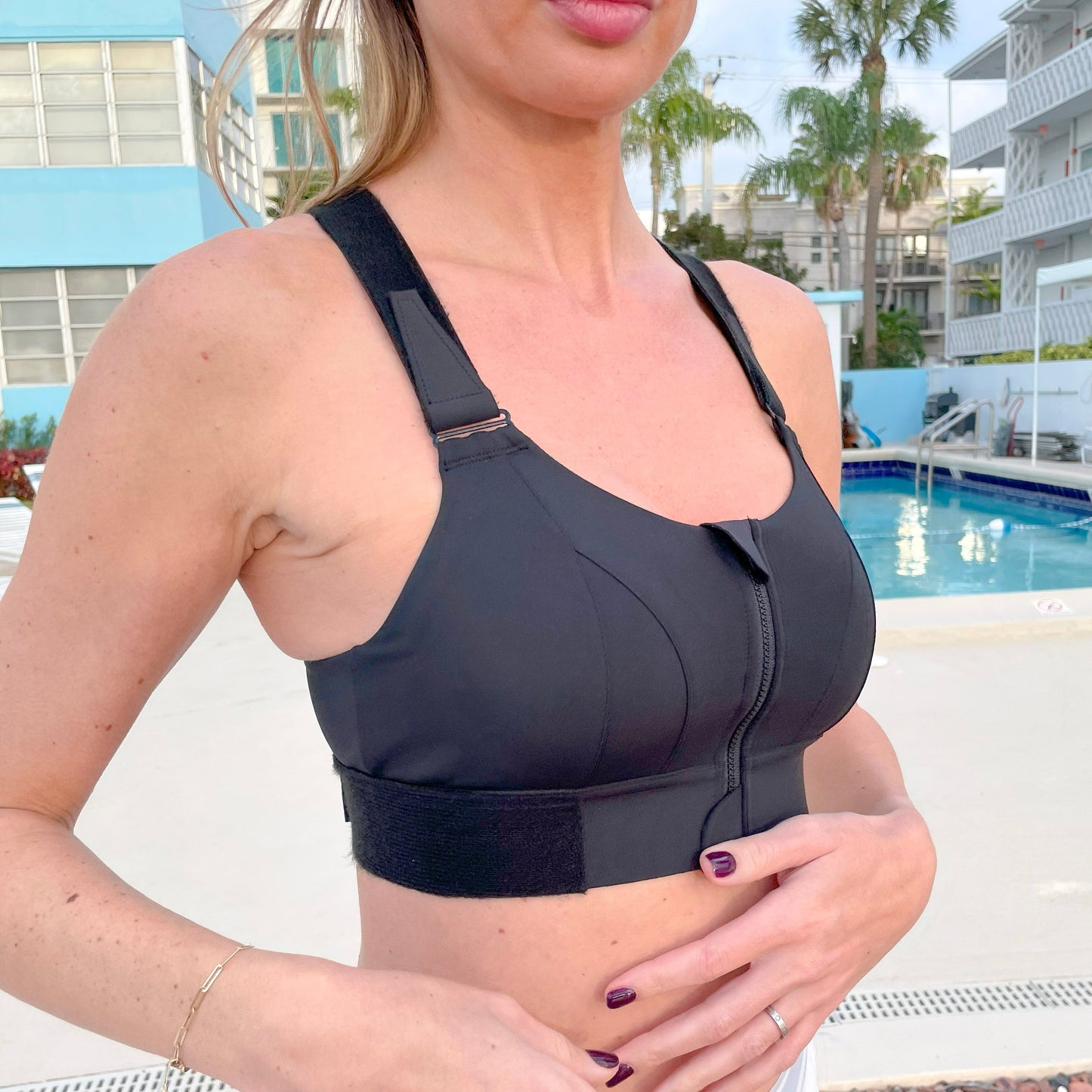 Slimming black Acadia high impact sports bra with shockproof compression for back support and belly control, worn outdoors near pool, available in sizes S to XL